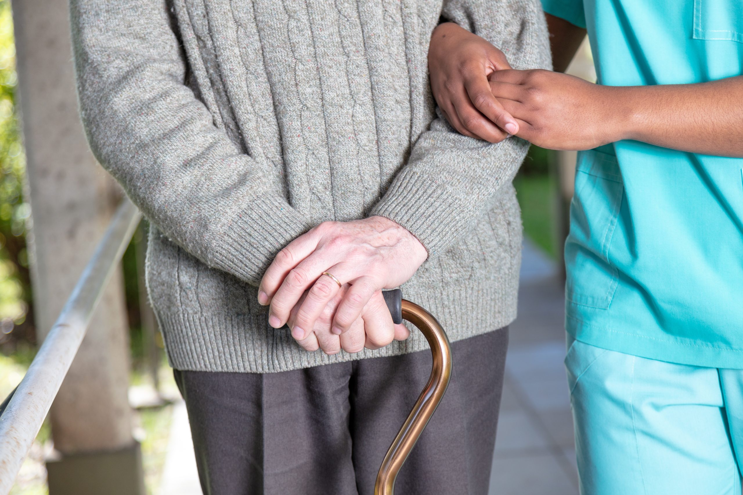 Elderly man with walking stick moving with nurse, detail on the hands.